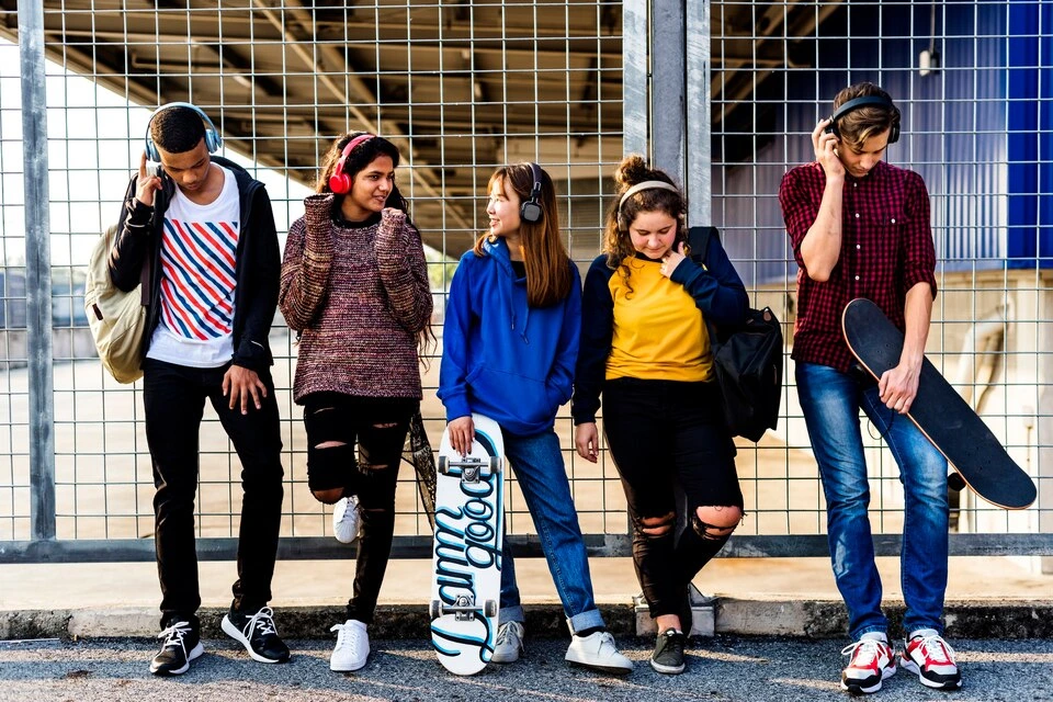 Group of diverse teens or high school students wearing headphones and modern, casual picture day outfits like jeans, hoodies, and jackets, with two students holding skateboards.